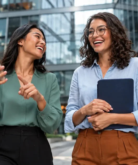 seguro D&O com duas profissionais sorrindo em um ambiente corporativo moderno, segurando celular e pasta, sugerindo confiança e gestão de risco no dia a dia