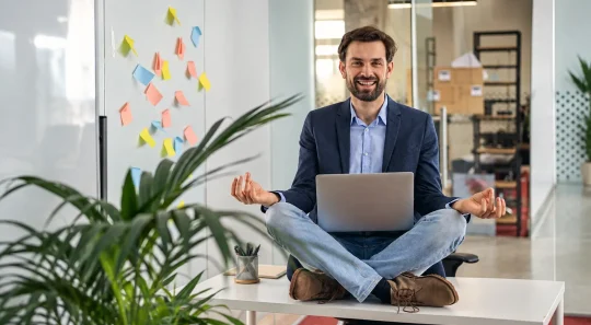 Homem sorridente trabalha em home office sentado na mesa com notebook, em um ambiente de escritório moderno com plantas e post-its coloridos; foco em saúde do colaborador