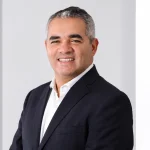 Retrato de Rodrigo Aguiar, superintendente Comercial e de Produtos da Seguros Unimed, sorrindo com os braços cruzados em cenário corporativo claro.